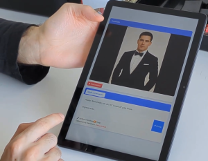 Tablet displaying a video chat interface with a man in a black tuxedo as the avatar, and blue chat/action bars visible on screen.