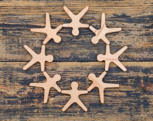 Wooden peg-figure silhouettes form a circle, holding hands on a weathered wooden surface.