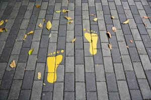 yellow footprints symbol on the floor - i-Healthcare Two yellow footprint illustrations painted on a grey brick sidewalk with scattered leaves around them.