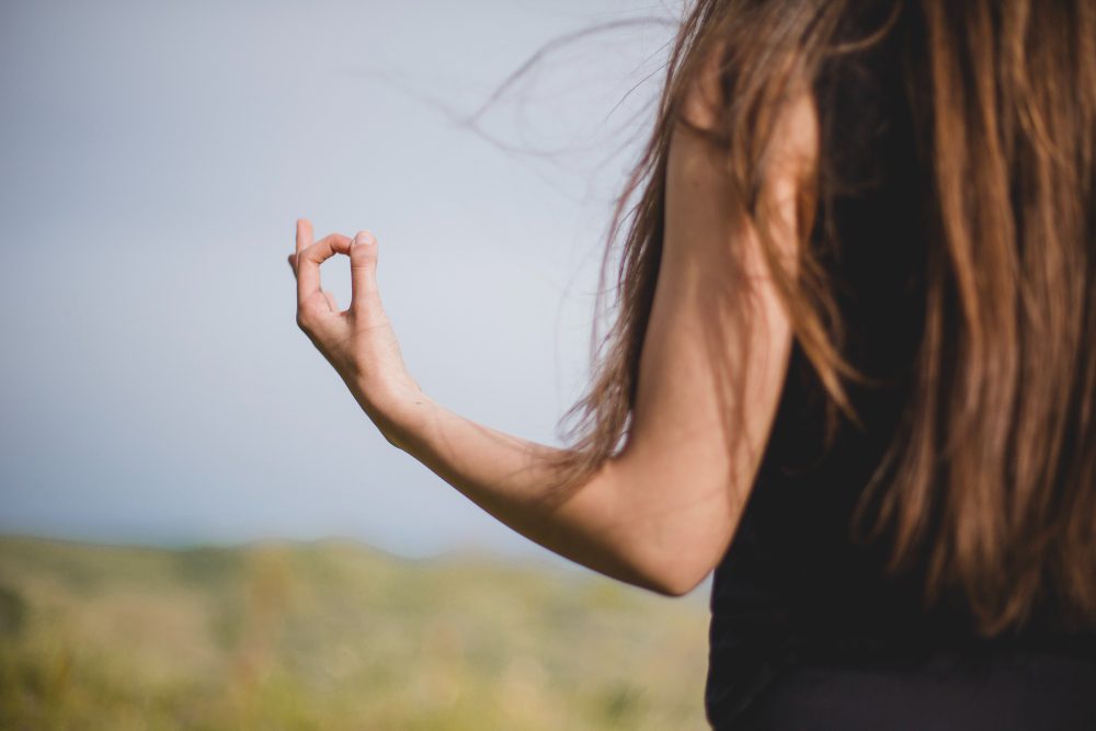 778460 - CAIP - i-Healthcare Person with long hair seen from behind outdoors, making an OK gesture with their hand against a blue sky.