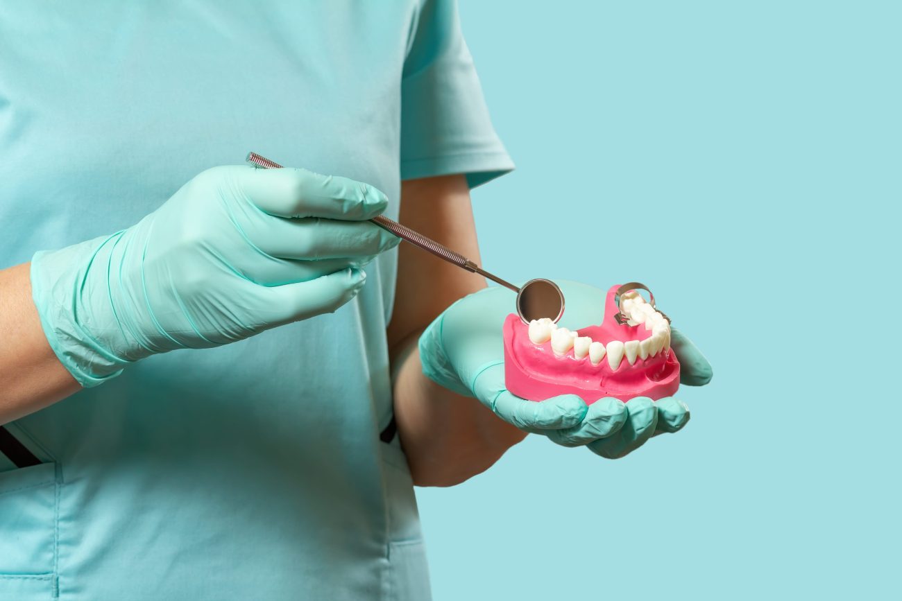 Dentist in latex glove with a layout of the human jaw and a mouth mirror - i-Healthcare